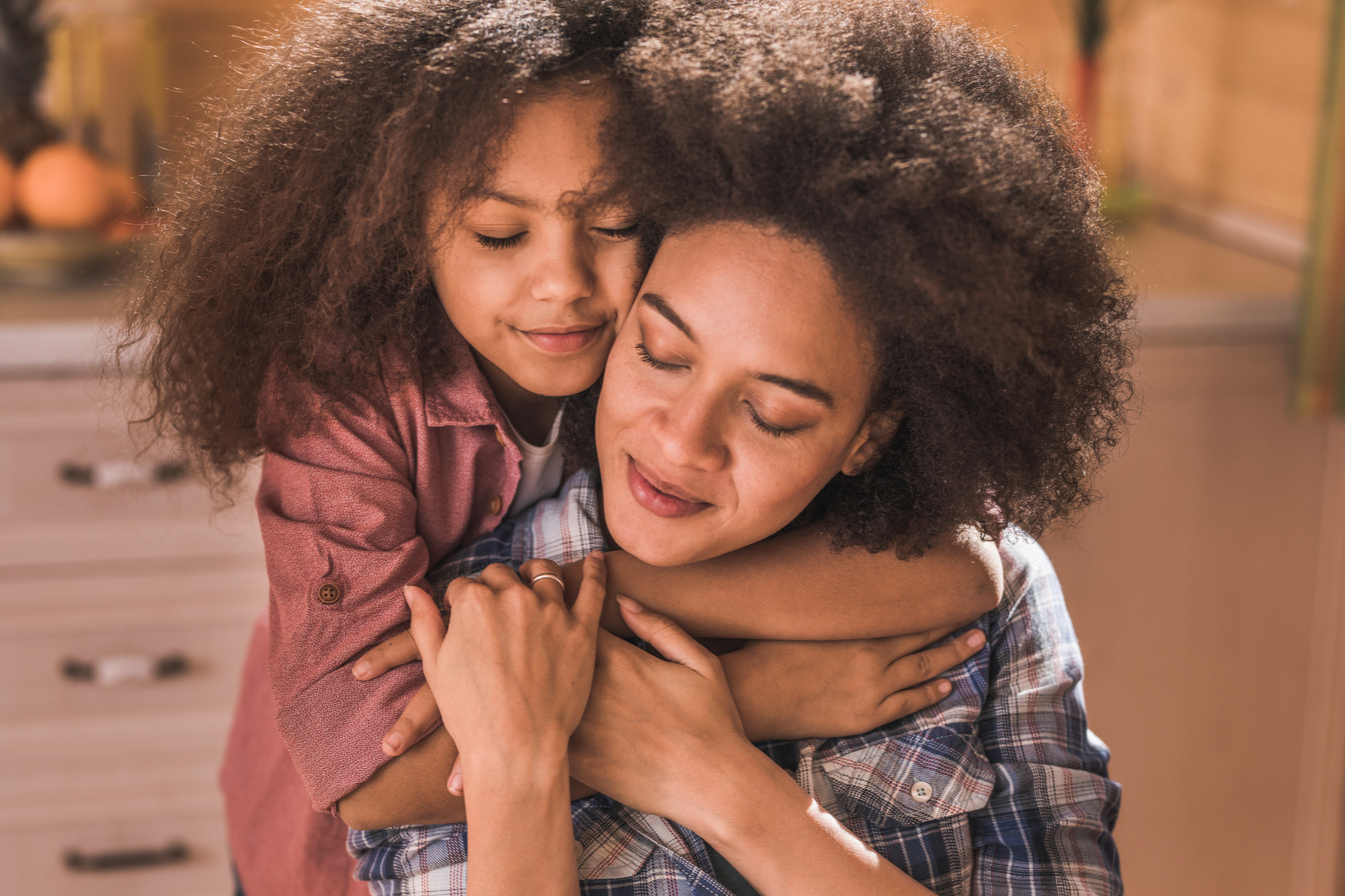 Affectionate black mother and daughter embracing with eyes closed.